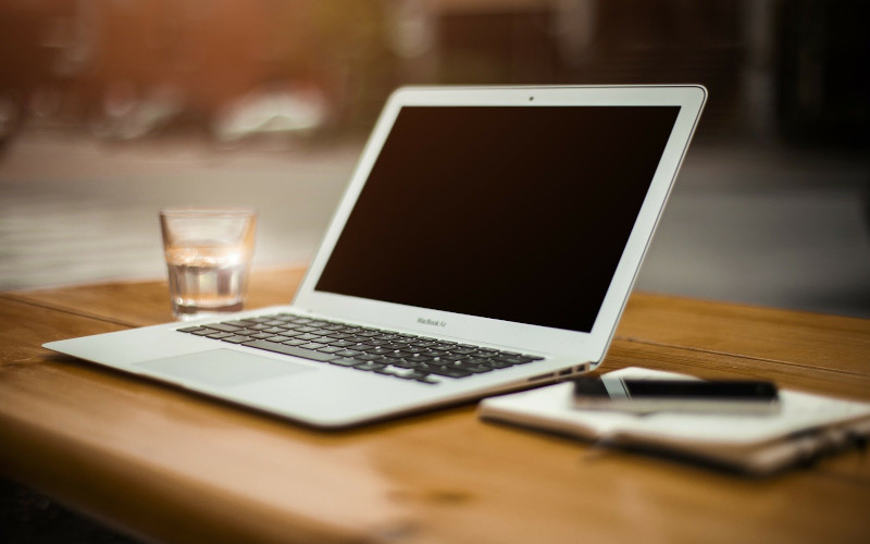 a laptop next to a notepad and a glass of water